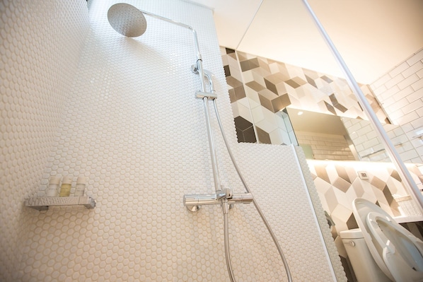 A modern bathroom with a textured white wall, a showerhead, and a toilet. - Stable Hotel (Tainan)