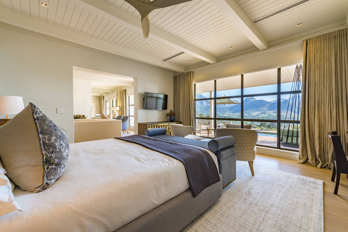 A modern hotel room with a large bed, a seating area with a view, and a television on the wall.