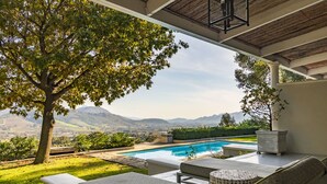 Área na piscina com vista para montanhas, uma árvore e mobiliário de exterior.