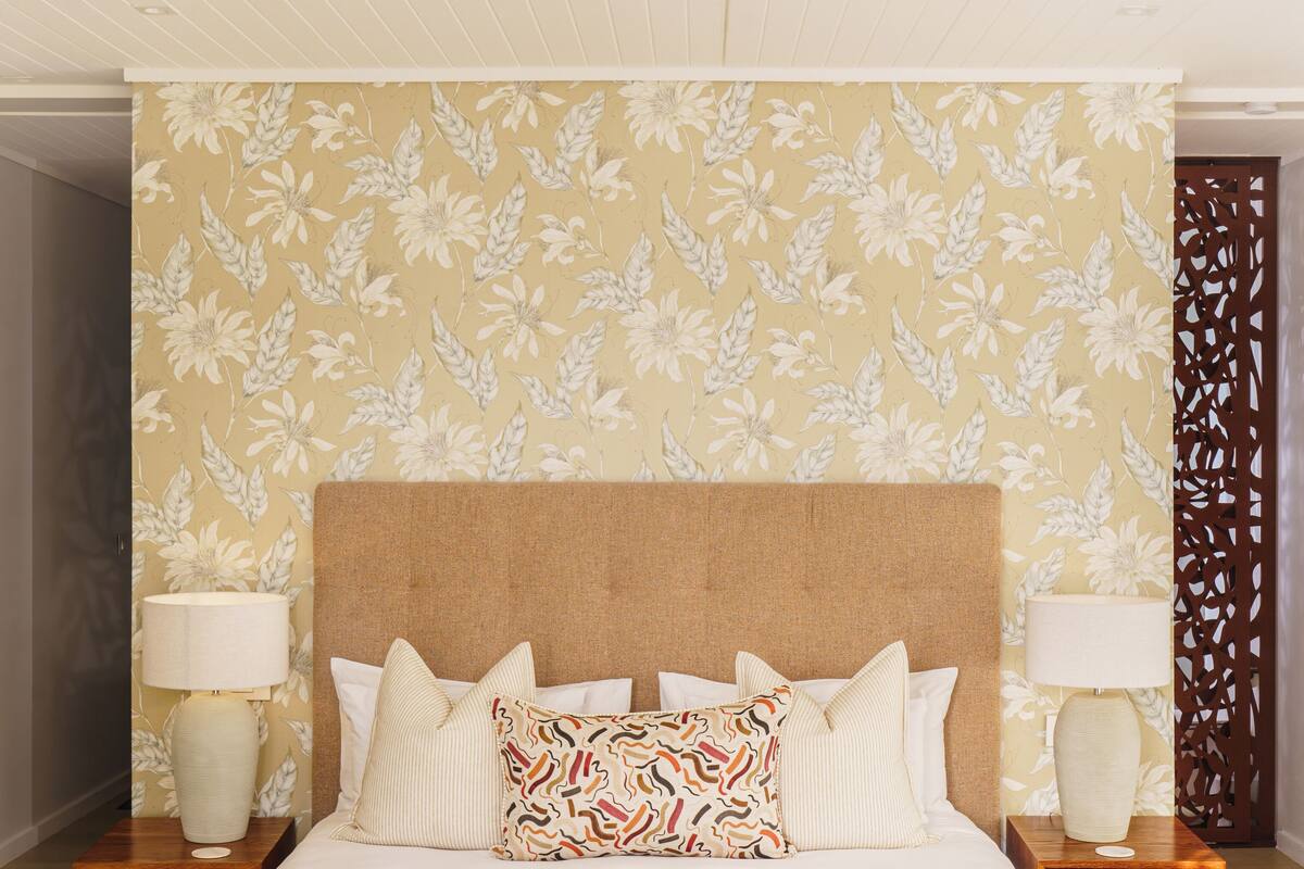 A large bed with a wooden frame, two nightstands with lamps, and a floral wallpaper pattern.