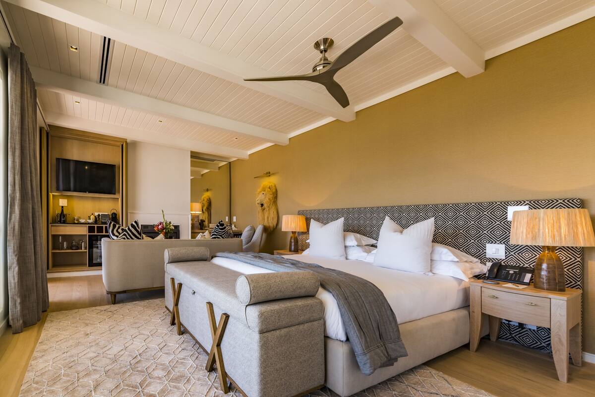 A modern hotel room with a large bed, a sitting area with a sofa, a desk, and a ceiling fan.
