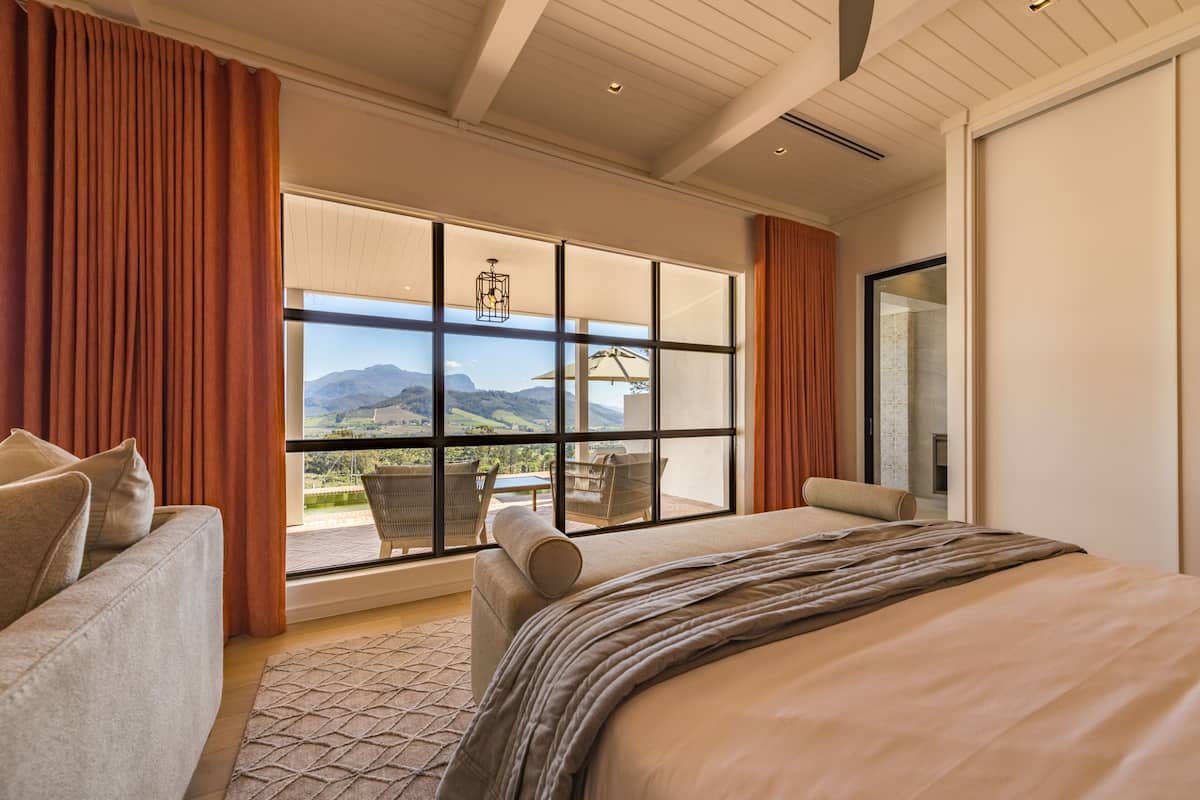 A bedroom with a large window, a bed, a sofa, and a view of mountains.