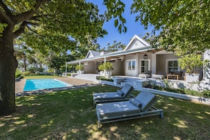 A modern house with a swimming pool, two lounge chairs, and a well-maintained lawn. - La Petite Ferme (Franschhoek)