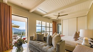 Quarto de hotel moderno com uma grande janela que oferece vista para a montanha, um sofá, uma cama e um ventilador de teto.