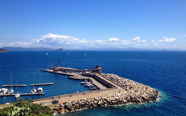 A coastal marina with boats docked, a rocky breakwater, and a clear blue sky.