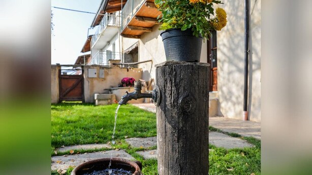 Un'elegante fontana esterna in stile rustico, con un pilastro in legno, un rubinetto in metallo e un vaso di fiori.