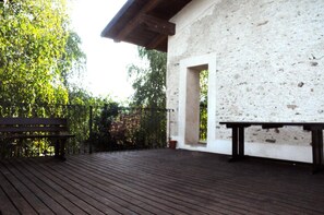 A wooden deck with a bench, a white building with a stone facade, and a metal gate. - Agriturismo Magnarosa (Barge)