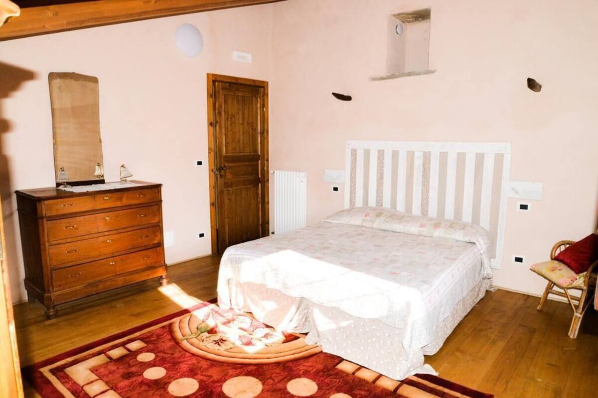 A bedroom with a wooden dresser, a bed with a white headboard, a red and beige patterned rug, and a small window.
