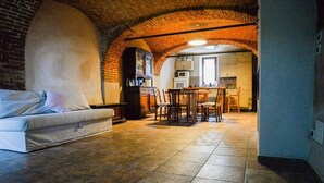Un accogliente soggiorno con divano, un tavolo da pranzo con sedie e una cucina visibile attraverso un soffitto in mattoni ad arco.