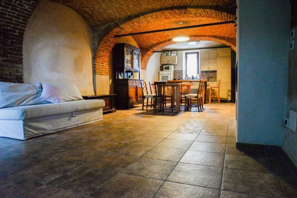 A cozy living room with a sofa, a dining table with chairs, and a kitchen area visible through an arched brick ceiling.