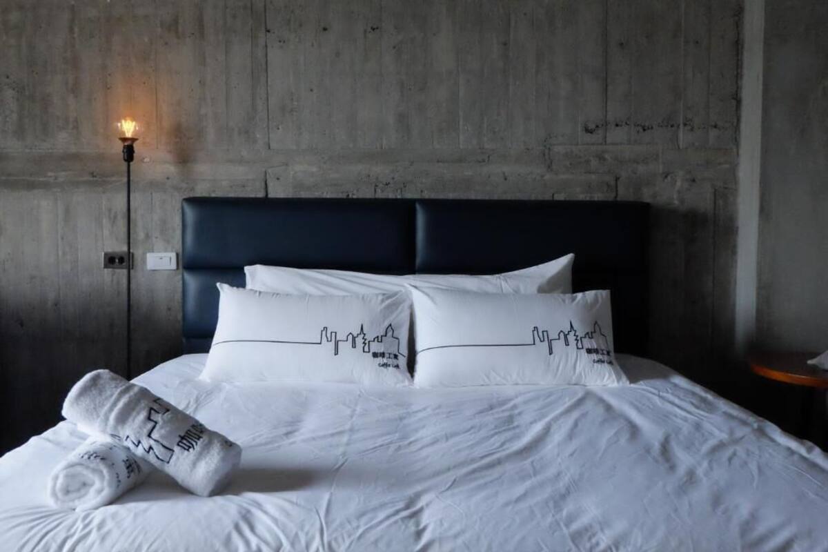 A hotel room with a bed, white linens, and a headboard.