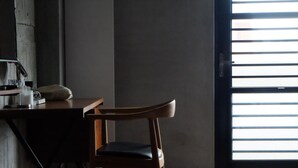 A wooden chair in a room with a dark floor, a table with a white object on it, and a window with horizontal blinds. - CoffeeLoft Inn &  Café (Taitung)