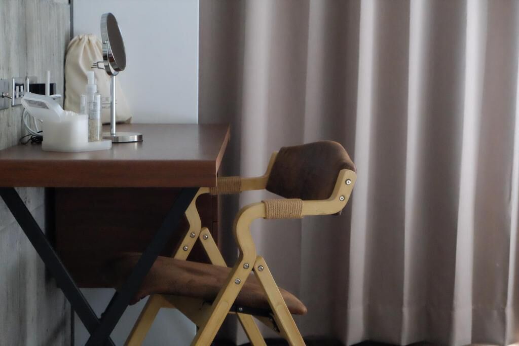 A wooden folding chair with a cushioned seat and backrest, positioned in front of a desk with a mirror and various personal items.