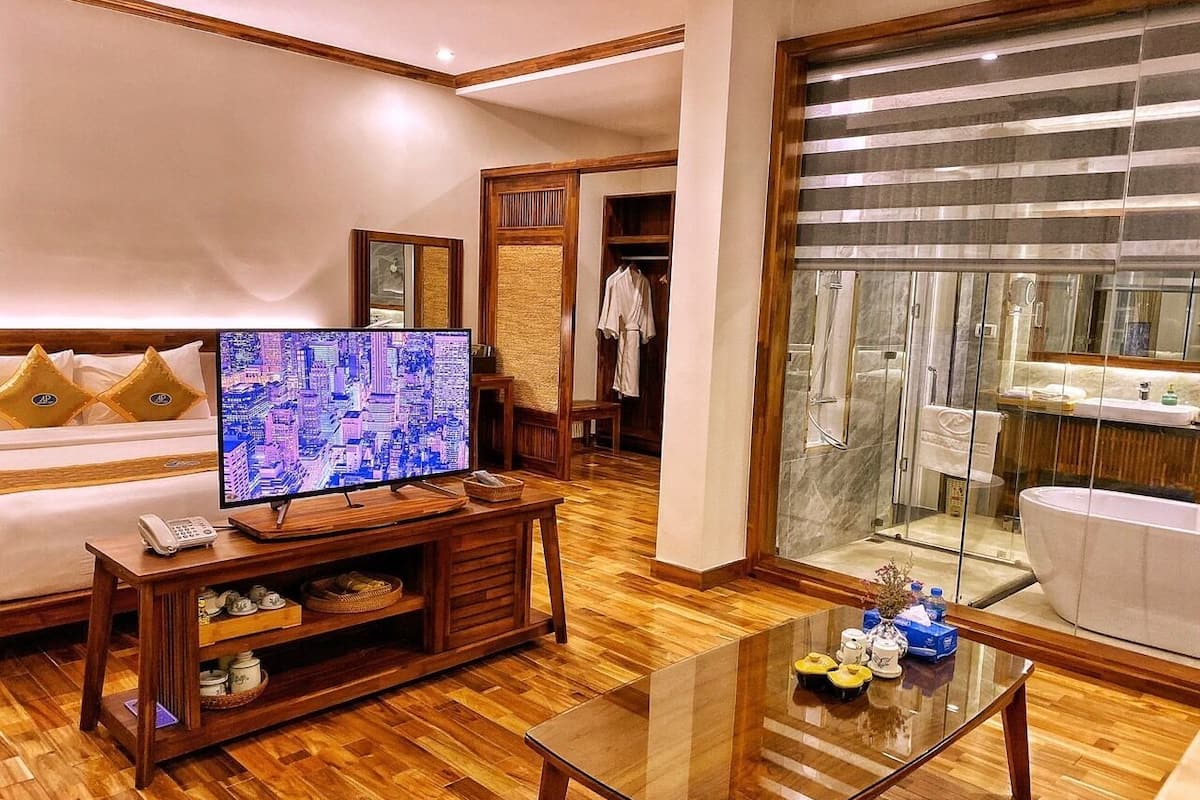 Een moderne woonkamer met een houten vloer, een glazen salontafel, een flatscreen televisie en een bank met decoratieve kussens.