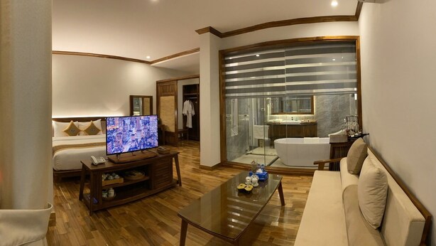 Een hotelkamer met televisie, bank, salontafel en een badkamer met bad en douche.