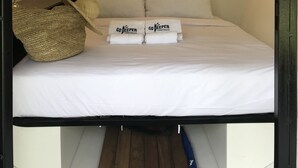 Um quarto pequeno e acolhedor com uma cama, almofadas, um cesto de vime e um ar condicionado fixado na parede.