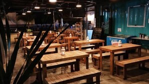 Um restaurante com mesas e bancos de madeira, uma parede azul e uma geladeira com freezer de sorvete Nestlé.
