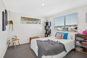 A bedroom with a bed, a bookshelf, a small table with a plant, and a window with blinds.