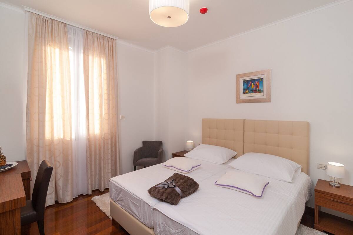 A hotel room with a bed, a chair, a desk, and a painting on the wall.