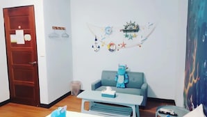 A room with a wooden door, a blue sofa, a small table with a tissue box, a wall decoration with nautical elements, and a trash bin. - Ching Yu Rou B&B (Dongshan)