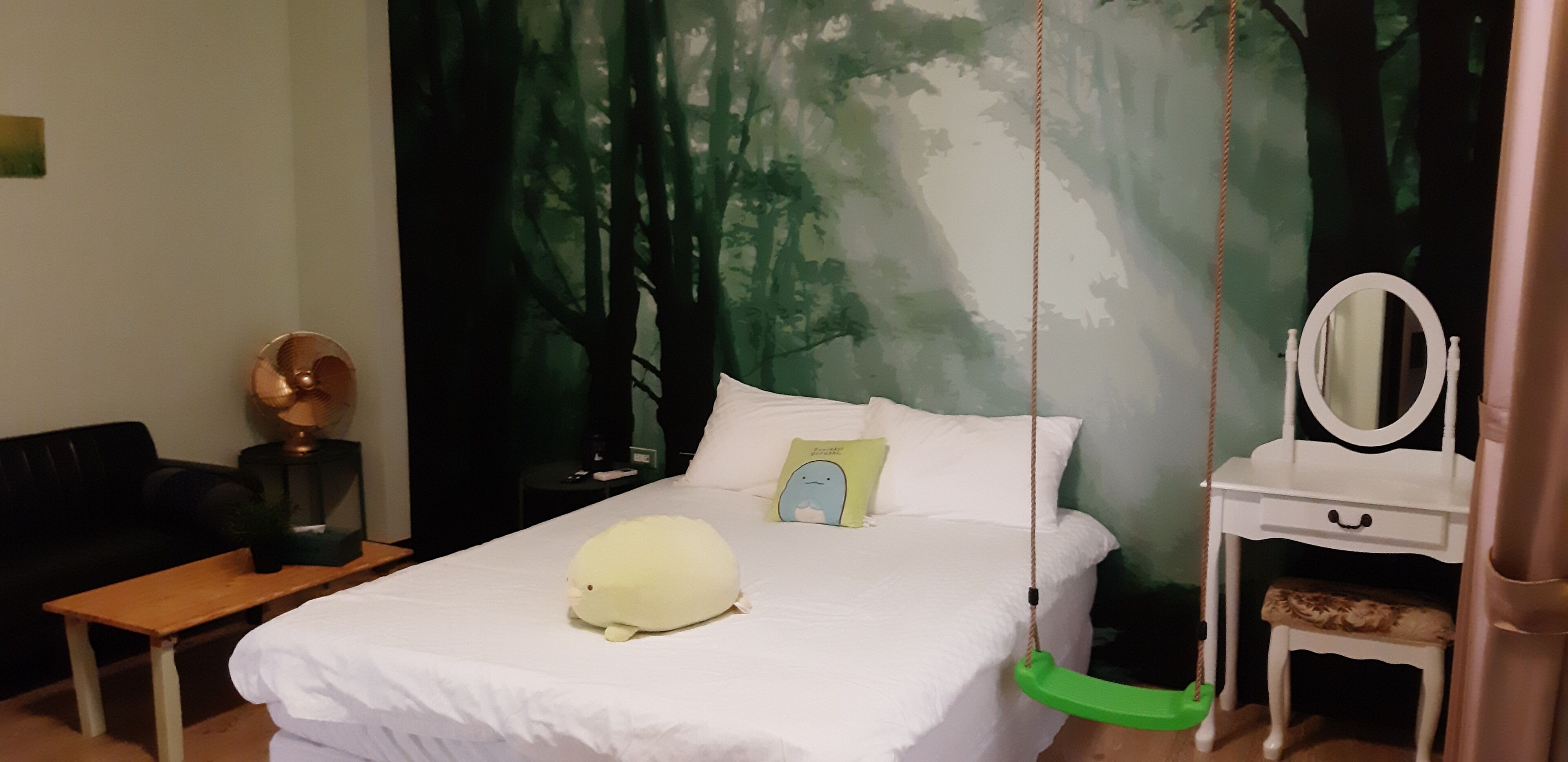 Un dormitorio con cama, una silla colgante, una mesita de noche con espejo y un mural en la pared.