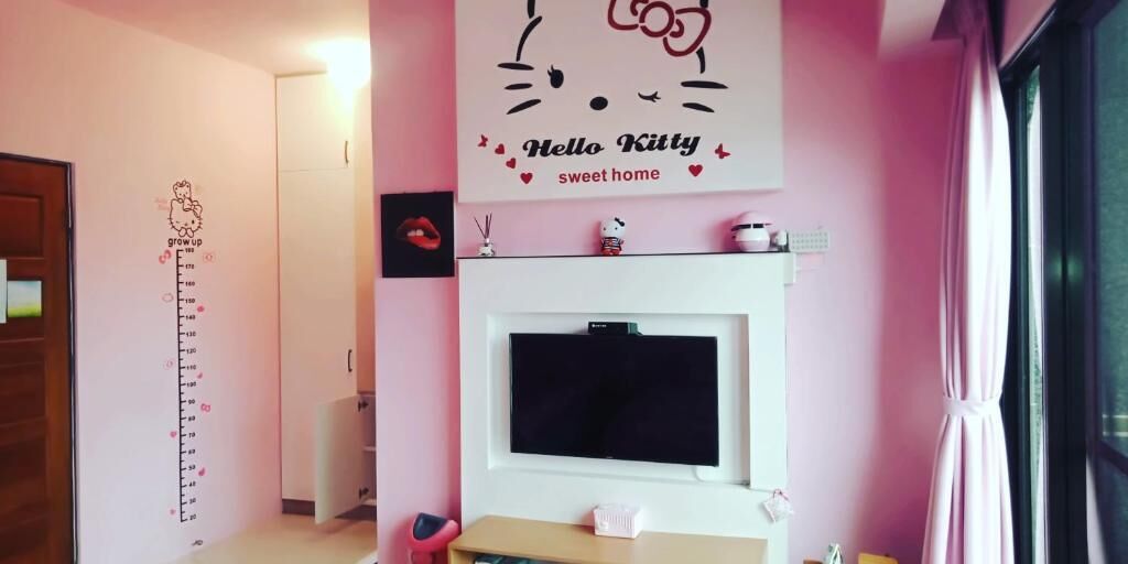 A pink-themed room with a 'Hello Kitty' wall decal, a TV, and a growth chart on the wall.