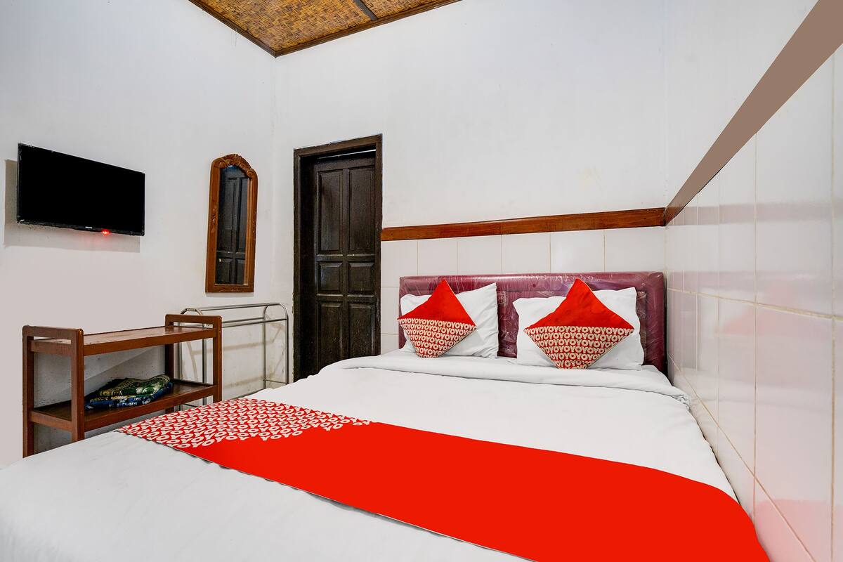 A hotel room with a bed, a TV mounted on the wall, a wooden door, and a small table with a chair.