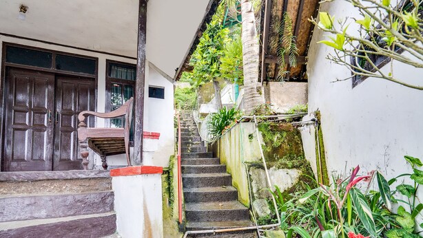A narrow staircase leading to a door with a wooden handrail, surrounded by greenery and a white wall. - OYO 2157 Pondok Gembyang Air Panas Alam (Rancabali)