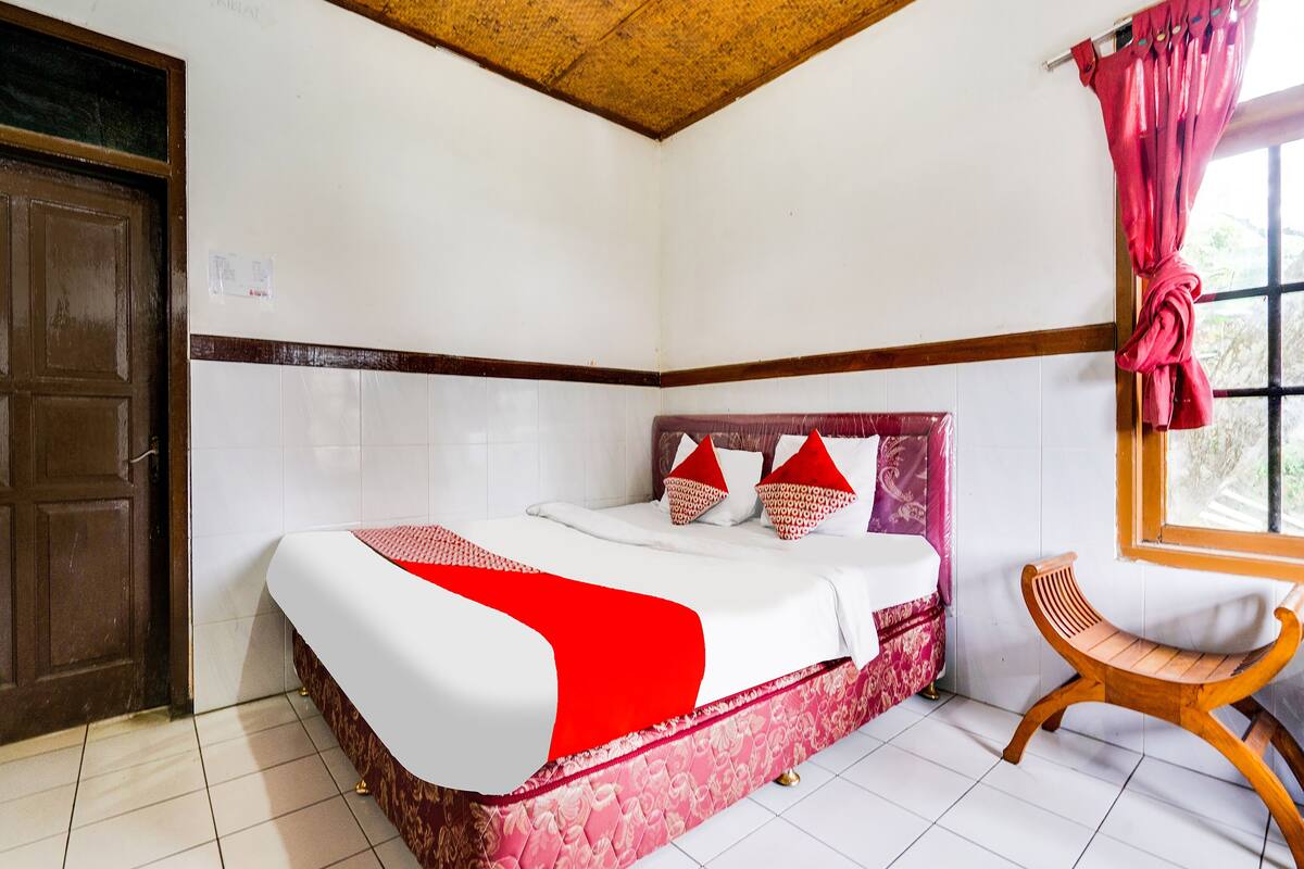A room with a bed, a wooden chair, a window with curtains, and a door.