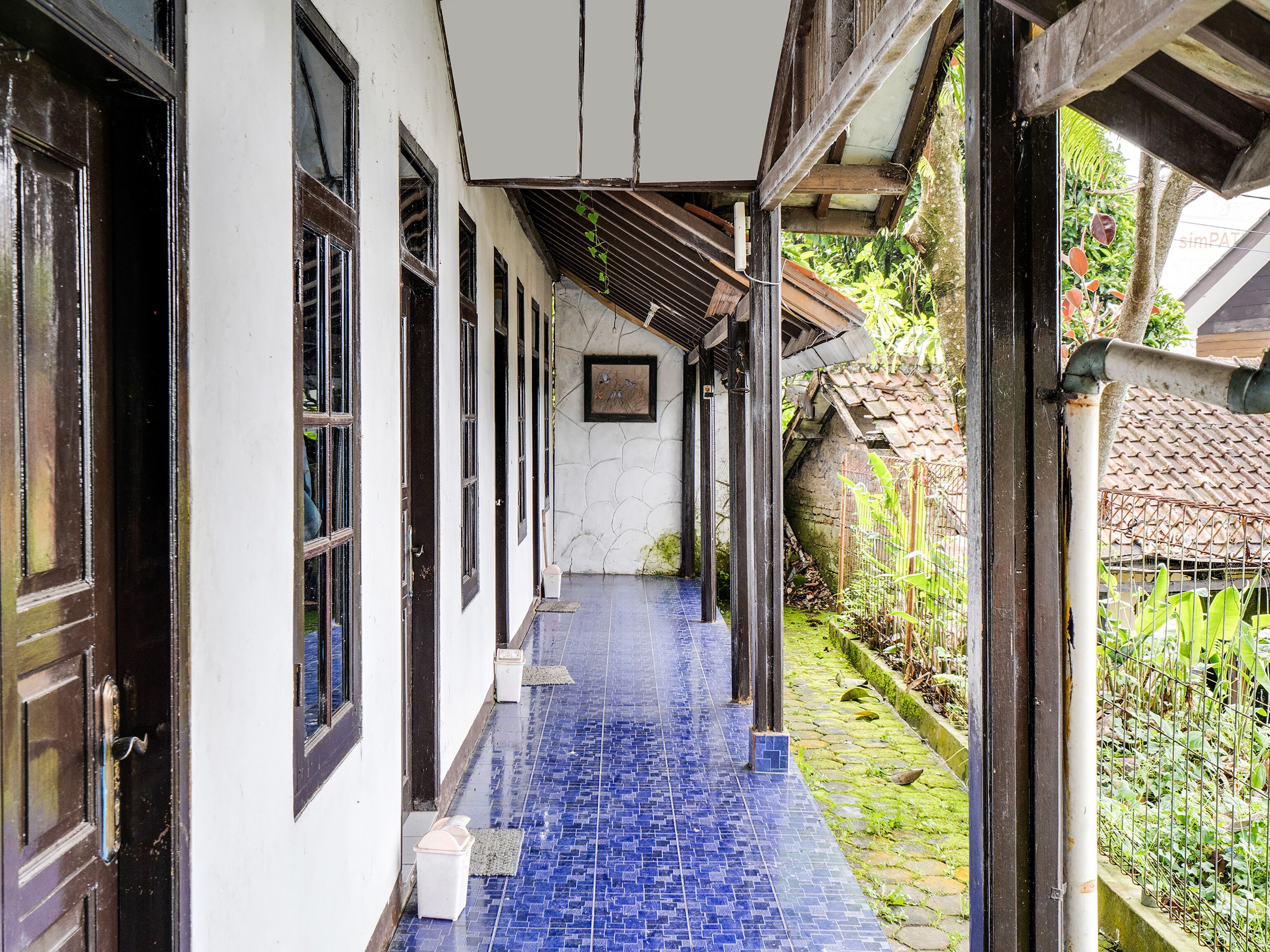 A corridor with tiled flooring and wooden doors, leading to a covered area with a tiled roof.