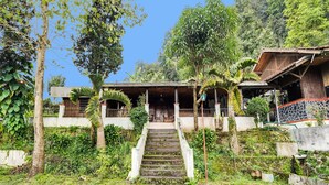A rustic building with a staircase leading to a covered porch, surrounded by lush greenery and trees. - OYO 2157 Pondok Gembyang Air Panas Alam (Rancabali)