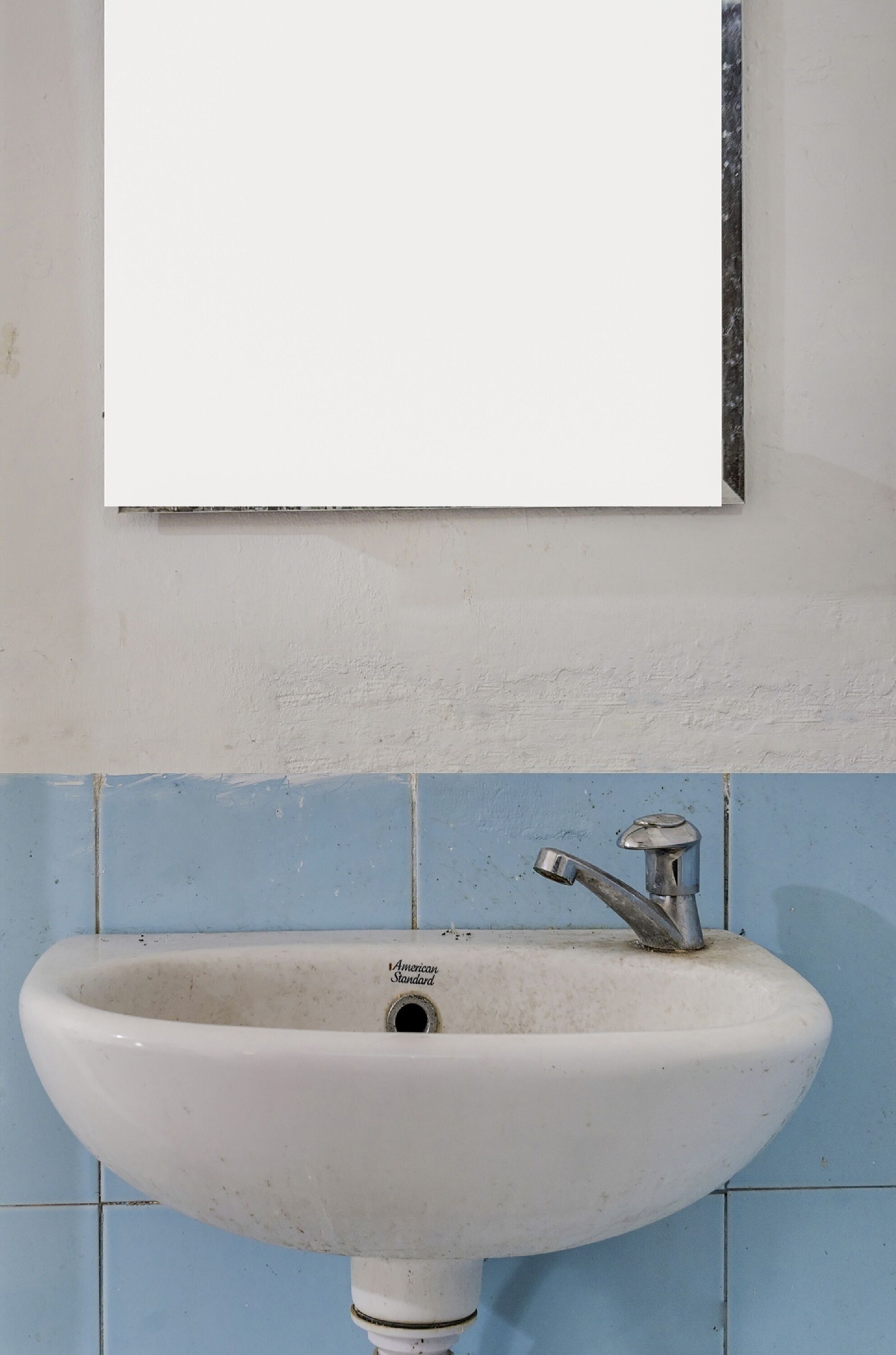 A white sink with a single faucet, mounted on a wall with blue tiles.
