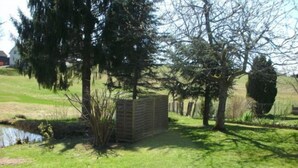 Une zone herbeuse avec un petit étang, une structure en bois et des arbres.