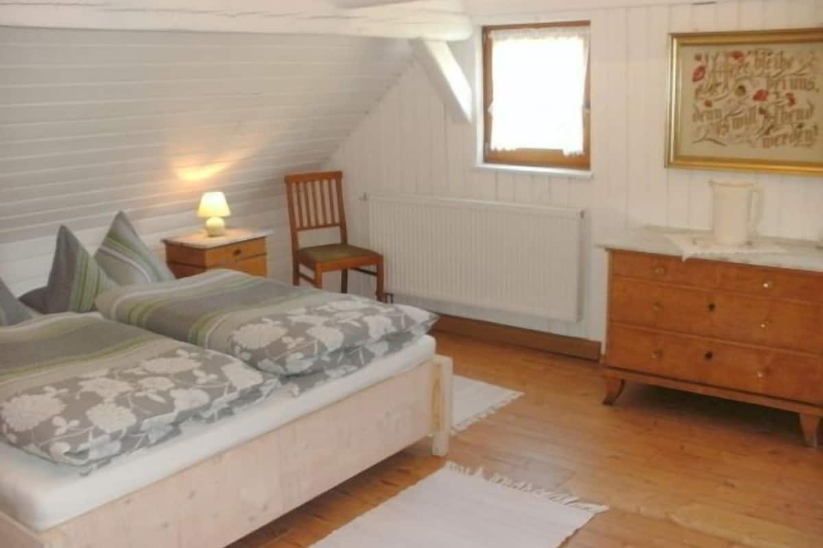 Een slaapkamer met een bed, een stoel, een dressoir, een radiator en een raam.