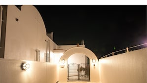 A nighttime view of a building's entrance with a gated archway, a light fixture, and a textured wall. - Seaside Tellme Ishigakizima (Ishigaki)