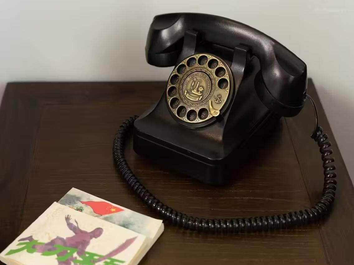 Un teléfono antiguo de disco giratorio negro sobre una mesa de madera.