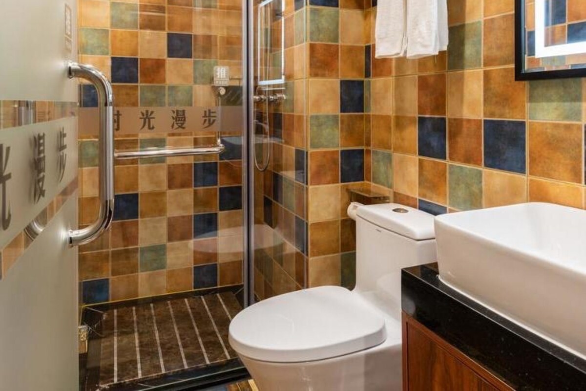 Un baño con cabina de ducha de vidrio, inodoro y lavabo con encimera negra.