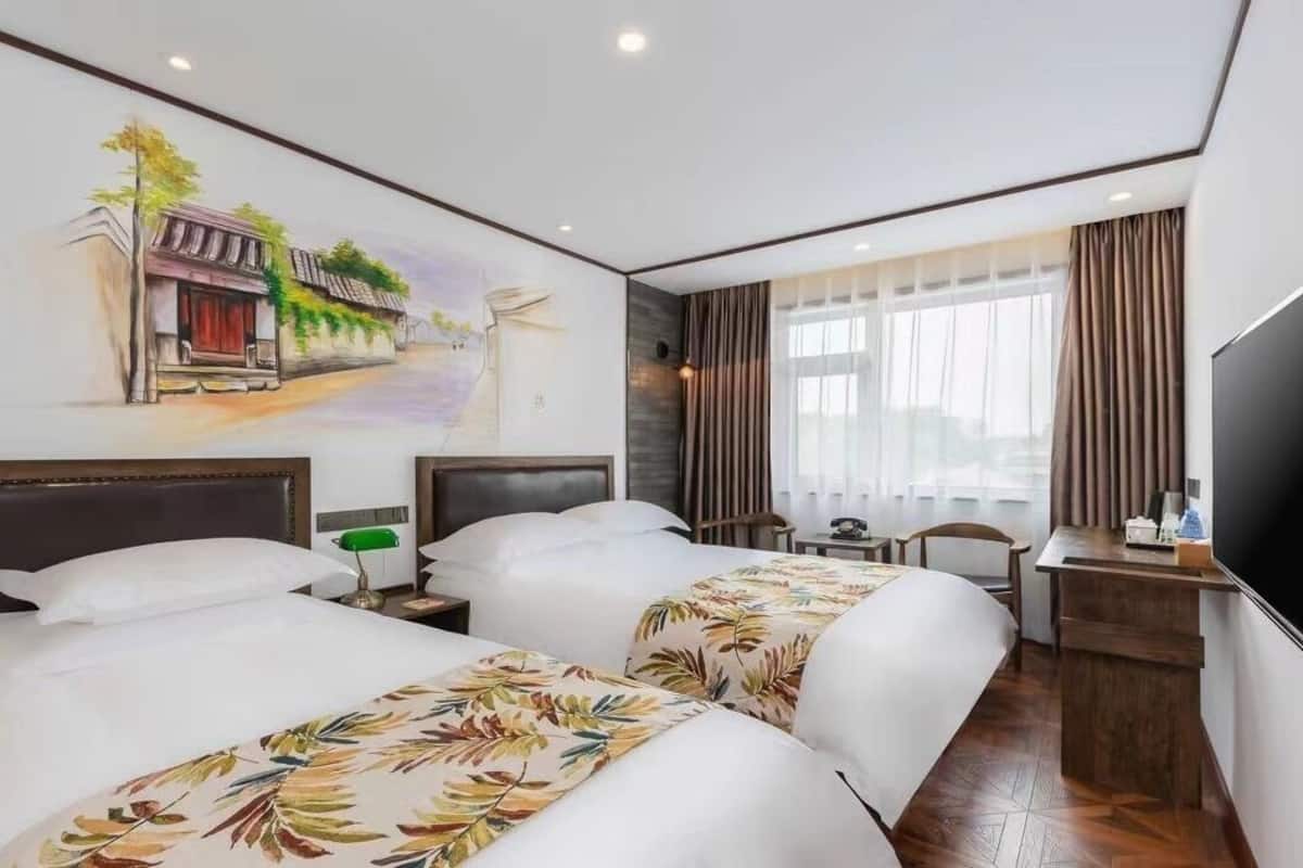 Een hotelkamer met twee bedden, een bureau, een televisie en een muurschildering.