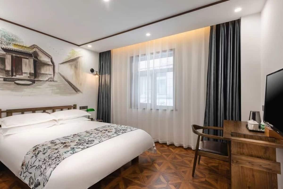 Een hotelkamer met een bed, een bureau met televisie en een groot raam met gordijnen.