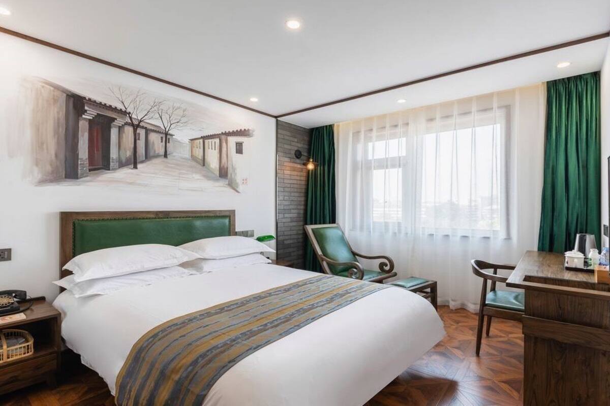 Een hotelkamer met een groot bed, een bureau, een stoel, een televisie en een schilderij aan de muur.