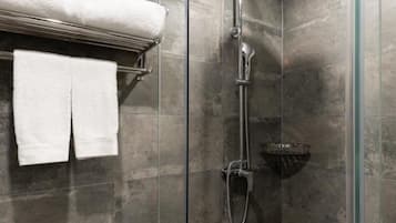Una ducha moderna con cabina de vidrio, un cabezal de ducha cromado y un perchero con dos toallas blancas.