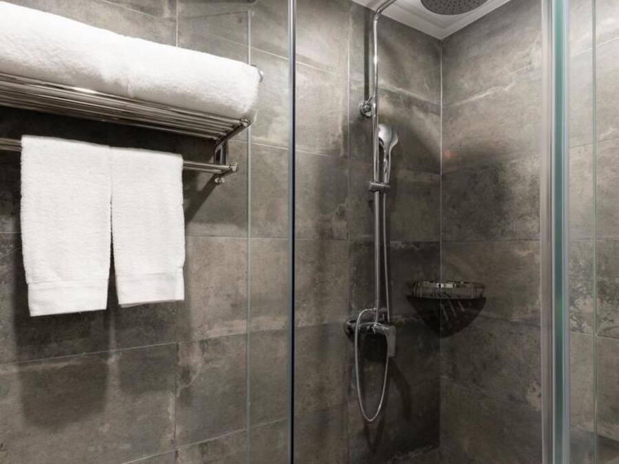 Una ducha moderna con cabina de vidrio, un cabezal de ducha cromado y un perchero con dos toallas blancas.