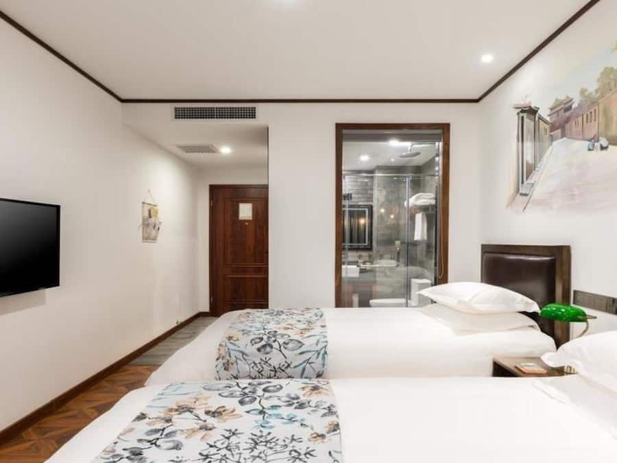 A hotel room with a TV, a bed with floral bedding, a bedside table with a green plant, and a shower area.