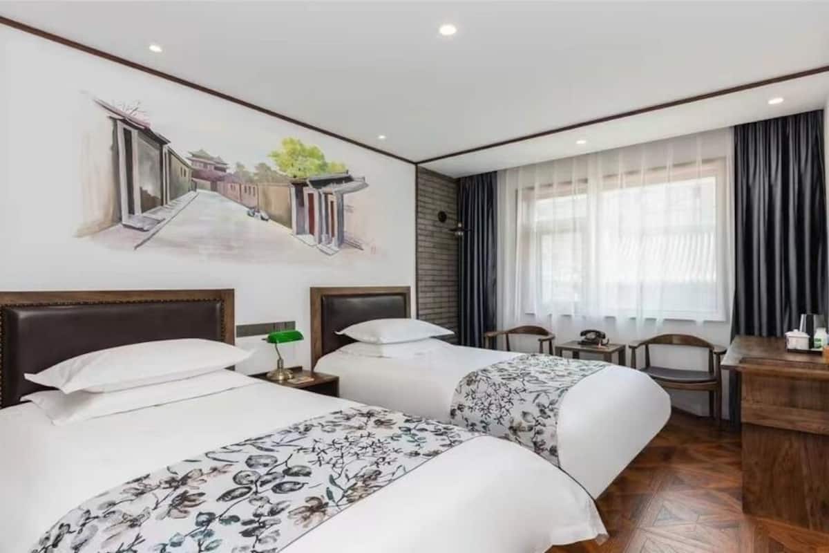 Hotelkamer met twee bedden, een bureau, een stoel, een televisie en een muurschildering.