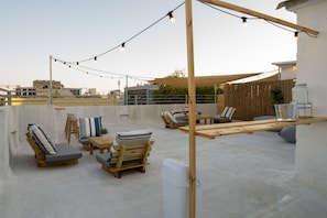 A rooftop terrace with wooden lounge chairs, a table, and string lights. - Meir's Boutique Guesthouse (Tel Aviv)