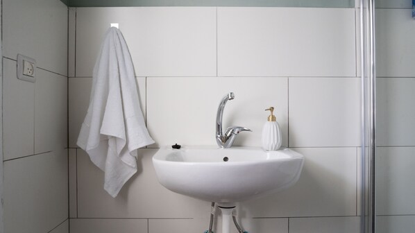 A bathroom with a white sink, a faucet, and a soap dispenser. A towel hangs on a hook to the left.