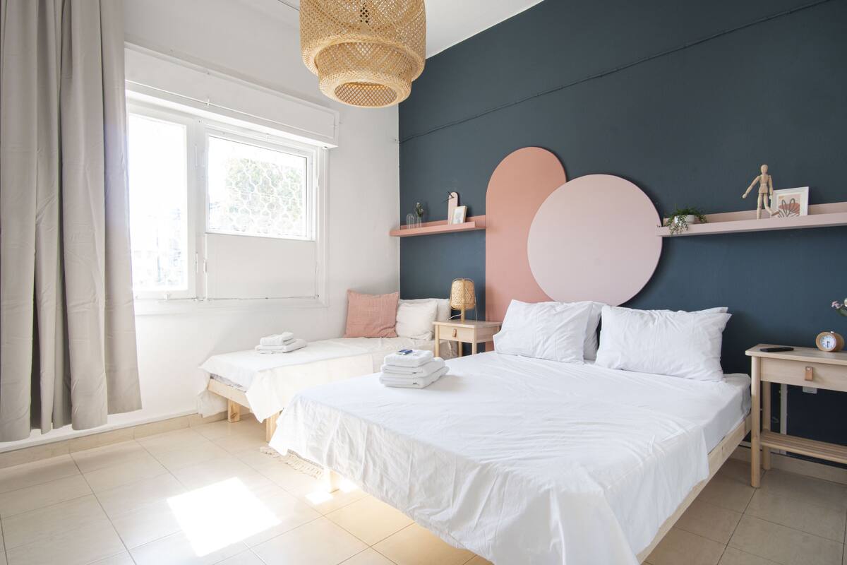 A modern bedroom with two beds, a large window, and a wall-mounted shelf with decorative items.