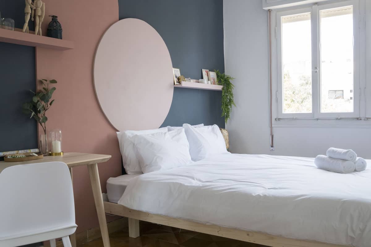 A bedroom with a bed, a desk, and a chair. There is a window with a view outside.