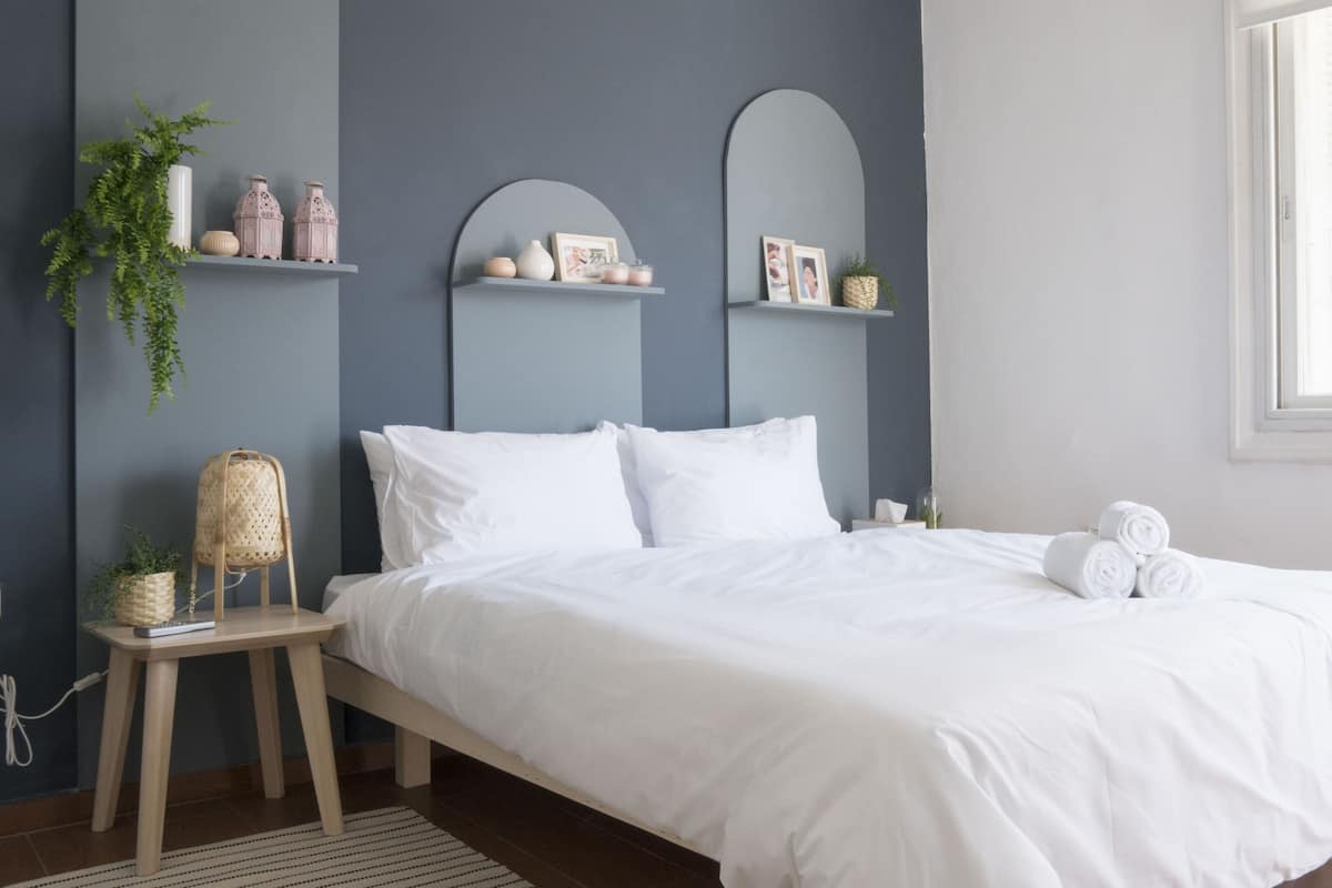 A neatly arranged bedroom with a bed, bedside tables, and shelves with decorative items.