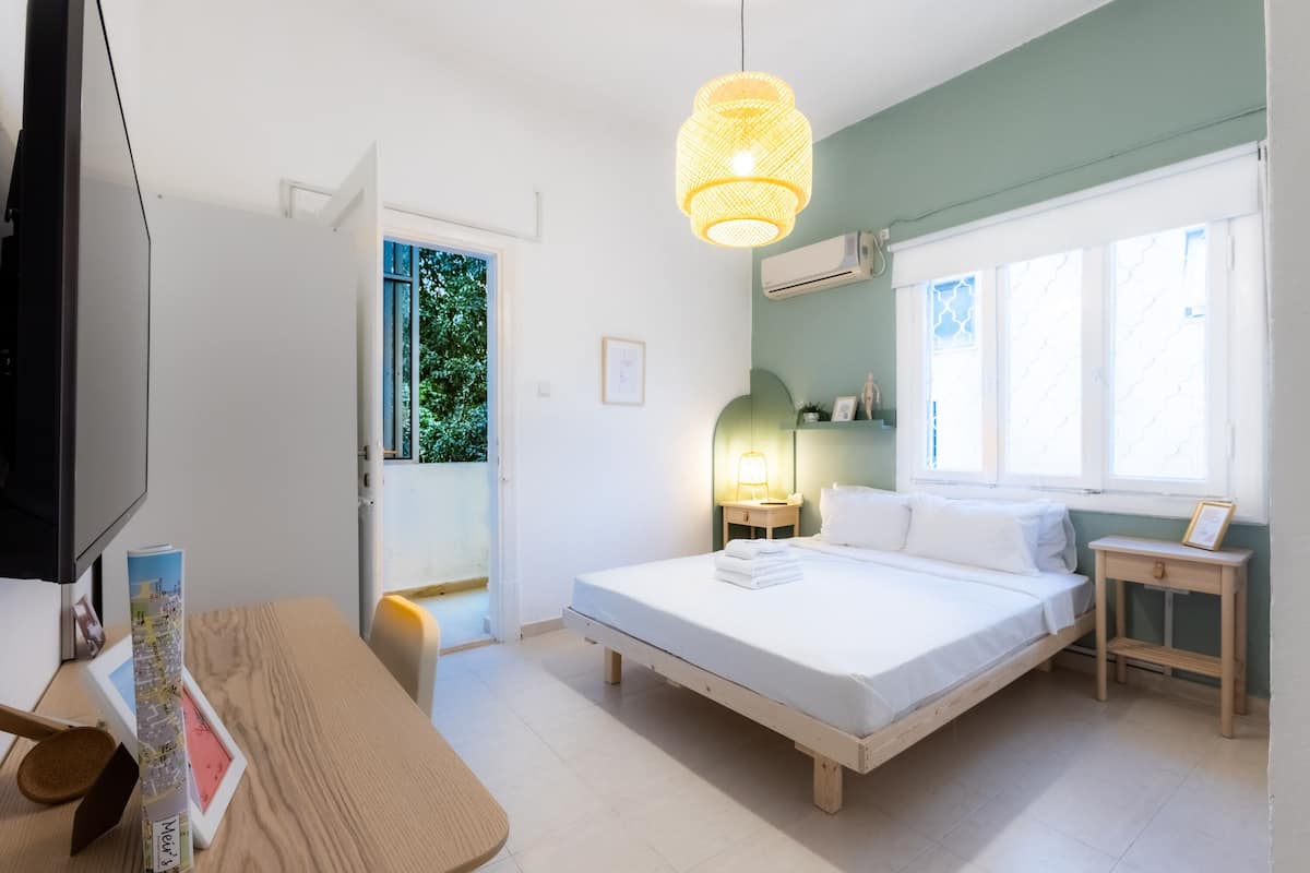 A bedroom with a bed, bedside tables, a lamp, a TV, and a window with a view of greenery.